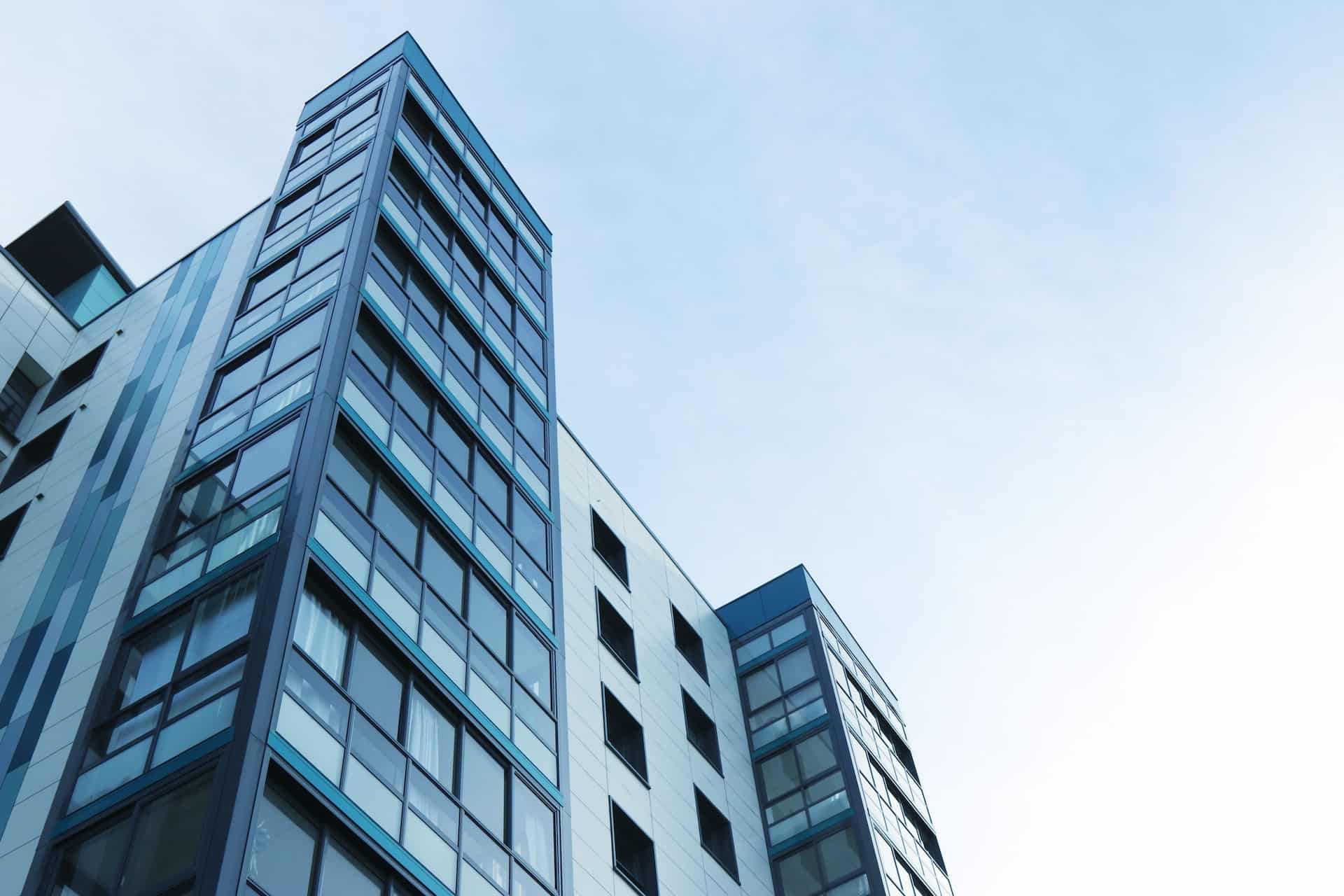 Low-angle view of a modern building with glass windows and light panels against a light blue sky.