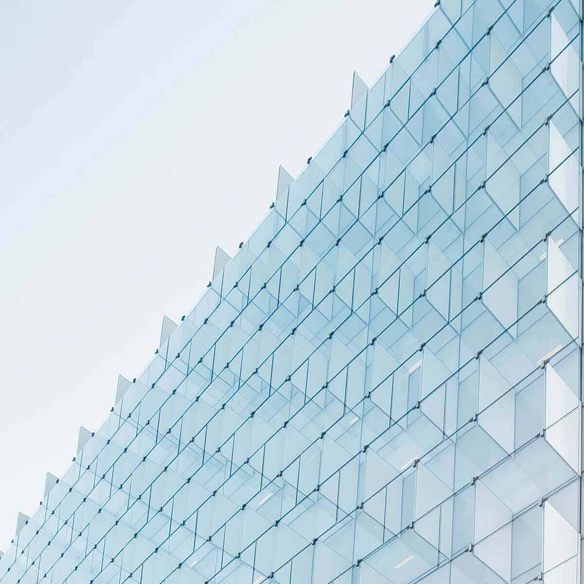 A close-up of a modern building facade with light blue glass panels arranged in a geometric grid against a clear sky.
