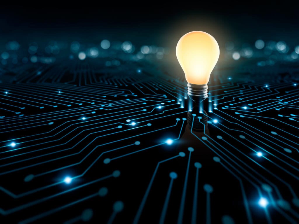 A glowing light bulb stands on a dark circuit board with illuminated blue traces and dots.