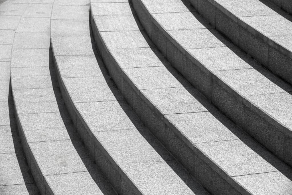 Curved light gray granite steps with strong diagonal shadows.