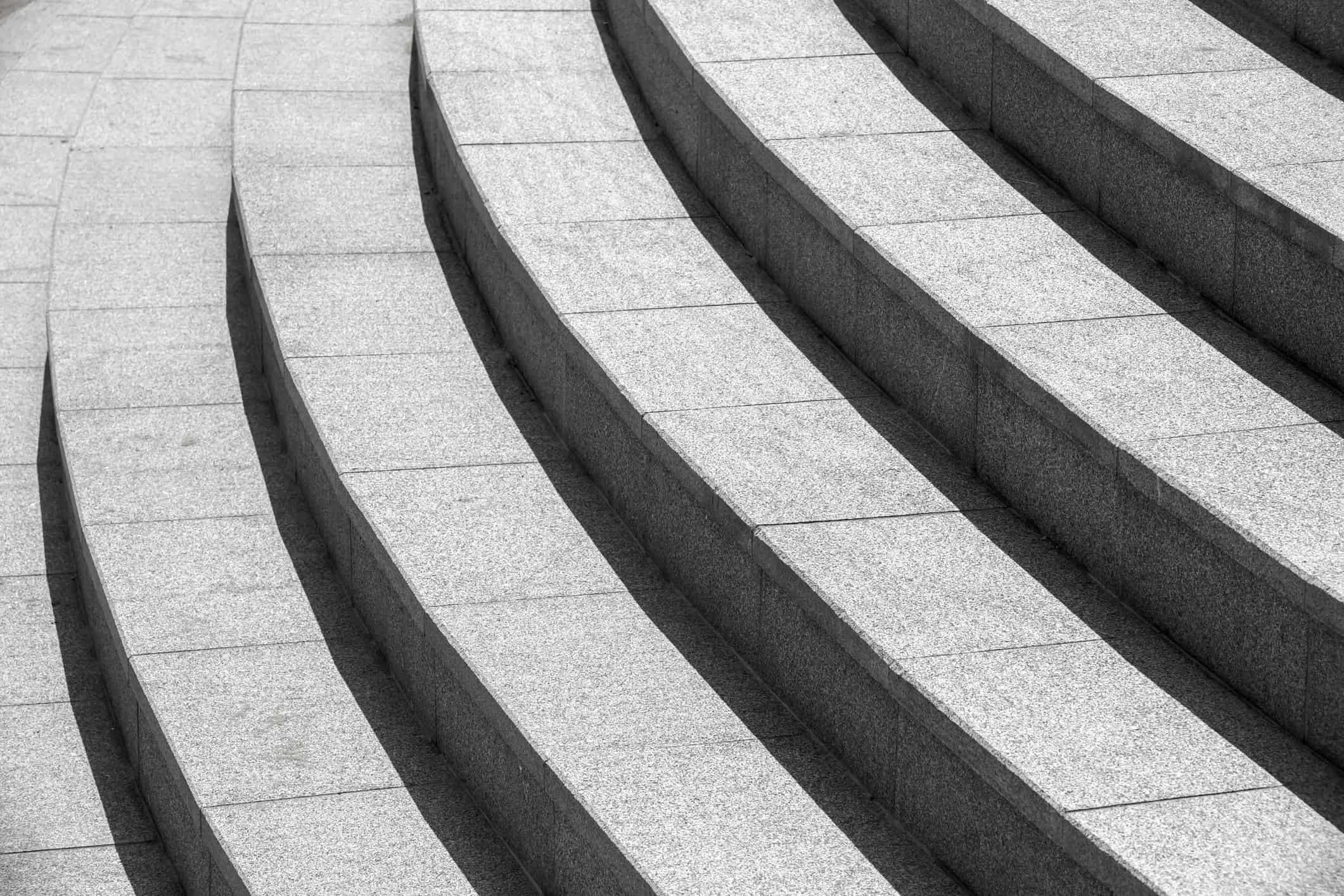 Curved light gray granite steps with strong diagonal shadows.