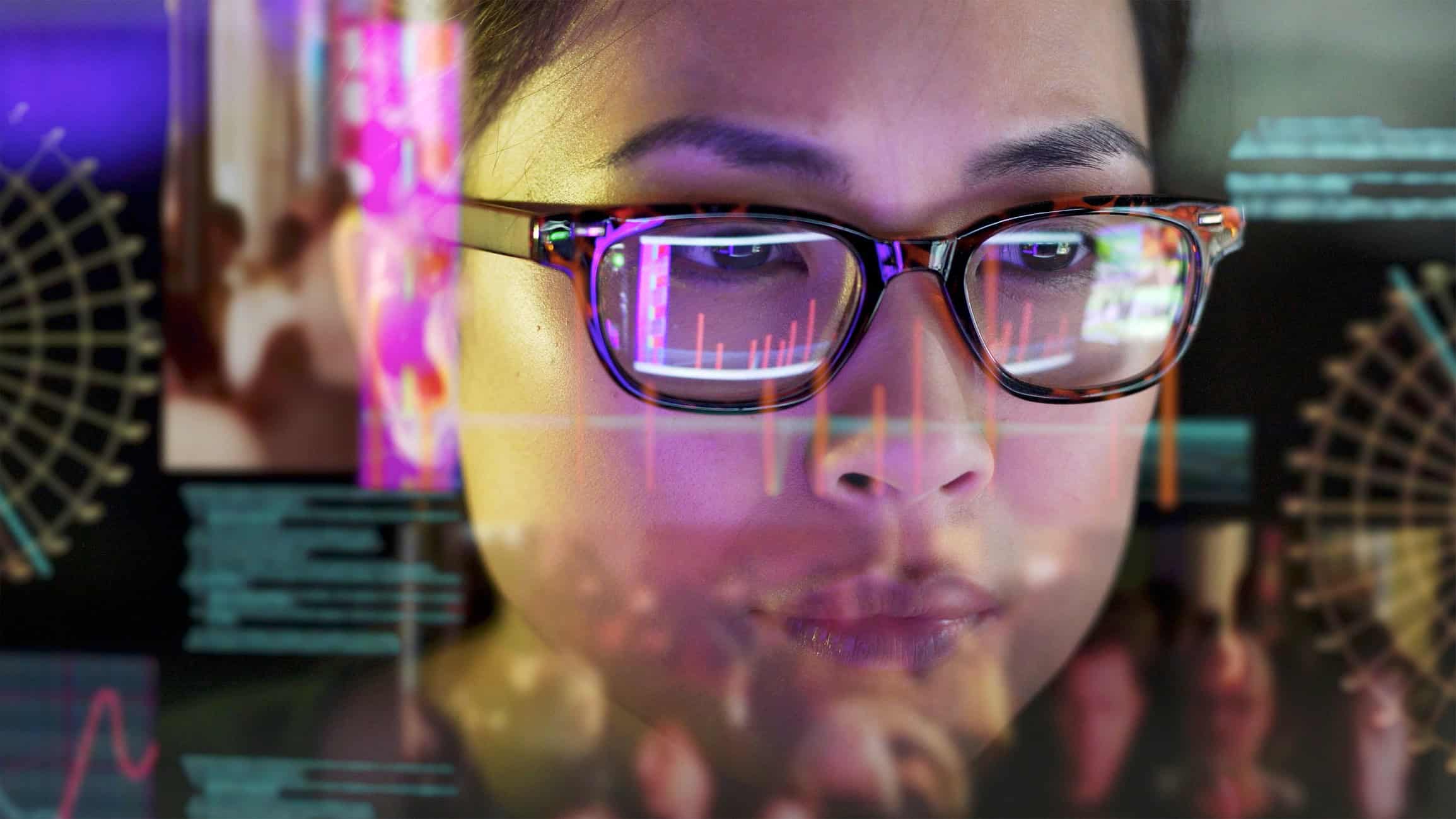 Close-up of a person wearing glasses, looking at a digital interface with data visualizations reflected in their lenses and overlaid on their face.