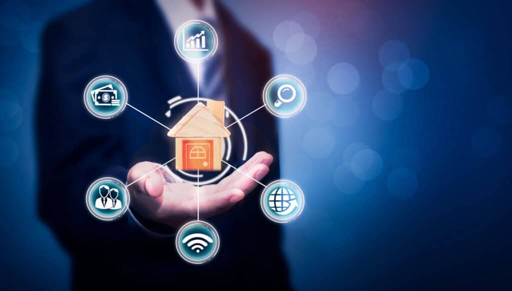 A hand holds a wooden house model, surrounded by glowing icons for finance, growth, search, global network, Wi-Fi, and people, against a blurred blue background.
