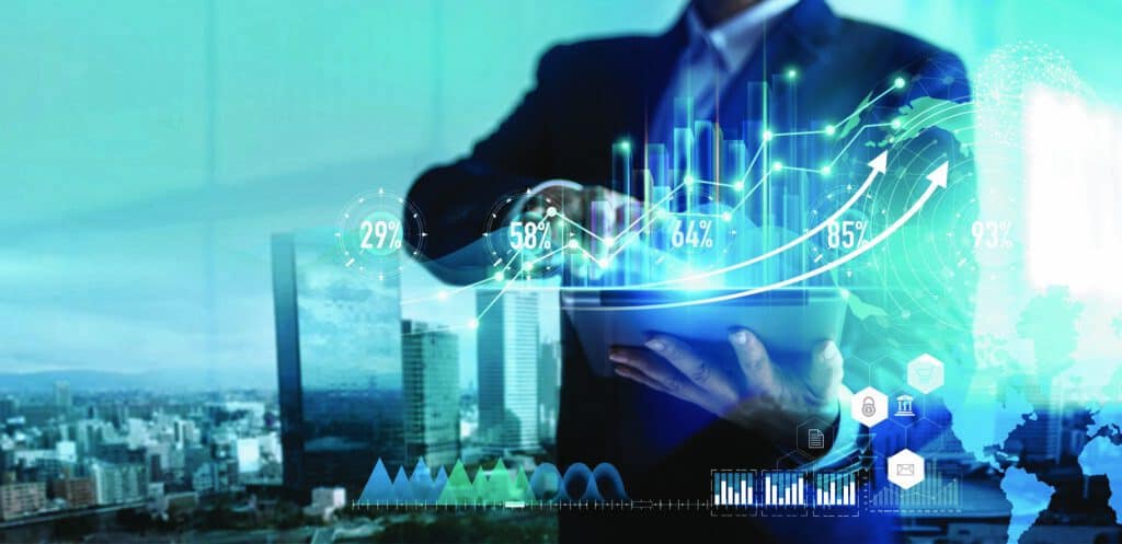A person in a suit holds a tablet, overlaid with digital graphs, percentages, a world map, and business icons, against a blurred city background.
