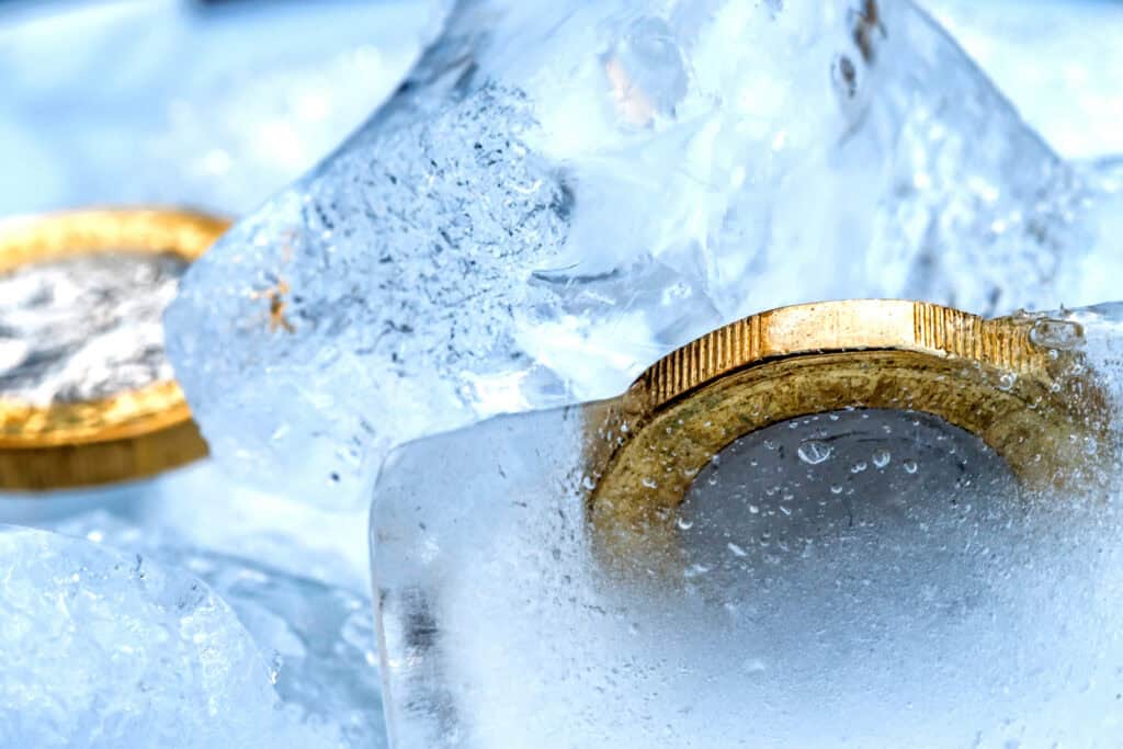 Close-up of two gold-colored coins, likely euro coins, frozen within clear, bubbly ice.