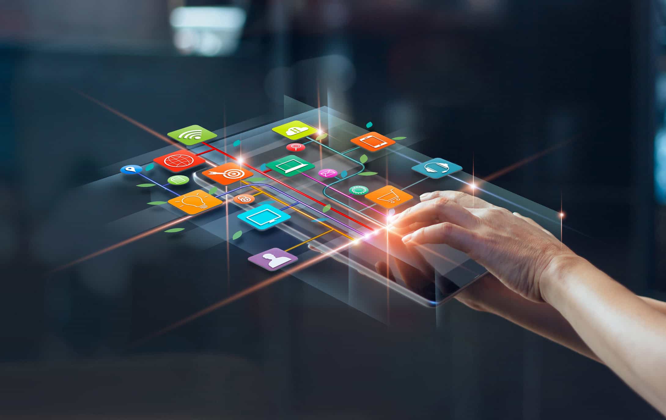 Hands interacting with a tablet displaying a glowing network of colorful application icons connected by lines.
