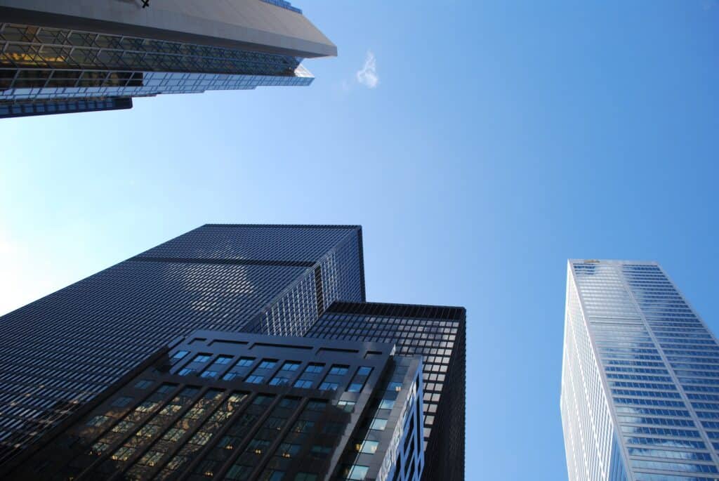 A worm's-eye view of multiple modern skyscrapers with glass and dark facades against a clear blue sky.