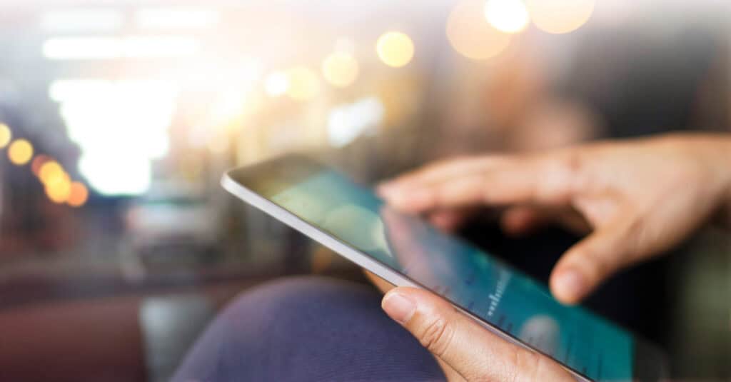 Close-up of hands using a tablet with a blurred background of warm lights.