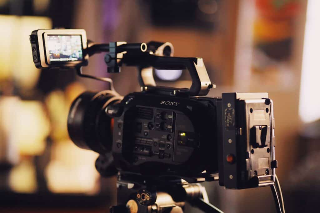 A black Sony XDCAM 4K video camera with an external monitor and large lens, mounted on a tripod in a softly lit, blurred indoor setting.