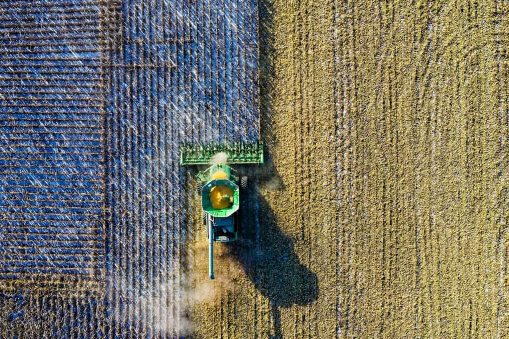 Aerial view of a green combine harvester cutting golden-yellow crops in a field, with harvested stubble visible on the left.