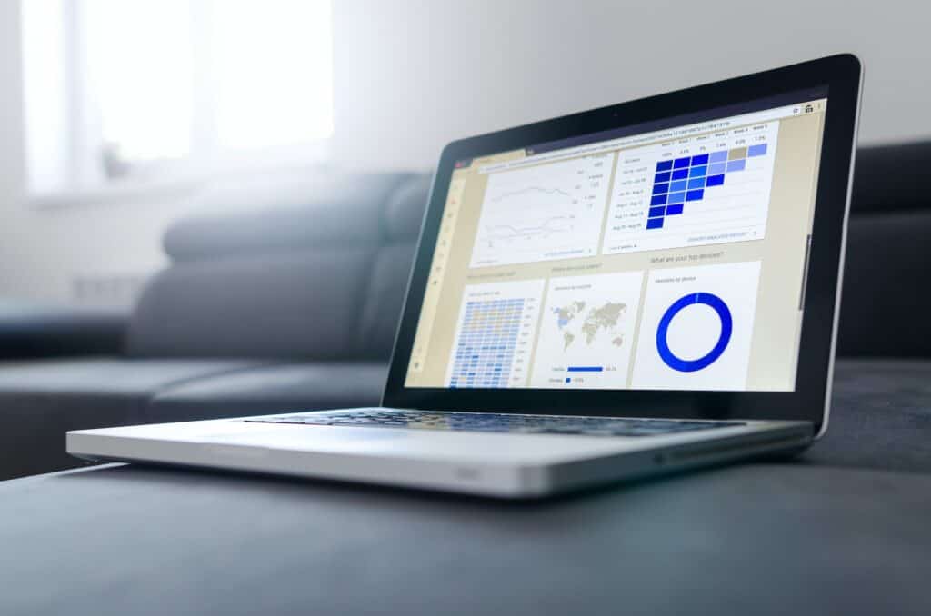 A silver laptop displaying data analytics reports, including user cohorts, geographic data, and device usage, resting on a dark gray sofa.