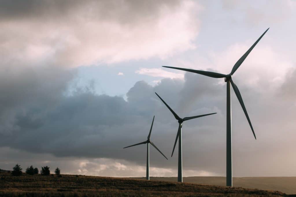 Three wind turbines on a grassy hill under a cloudy sky at sunrise or sunset.
