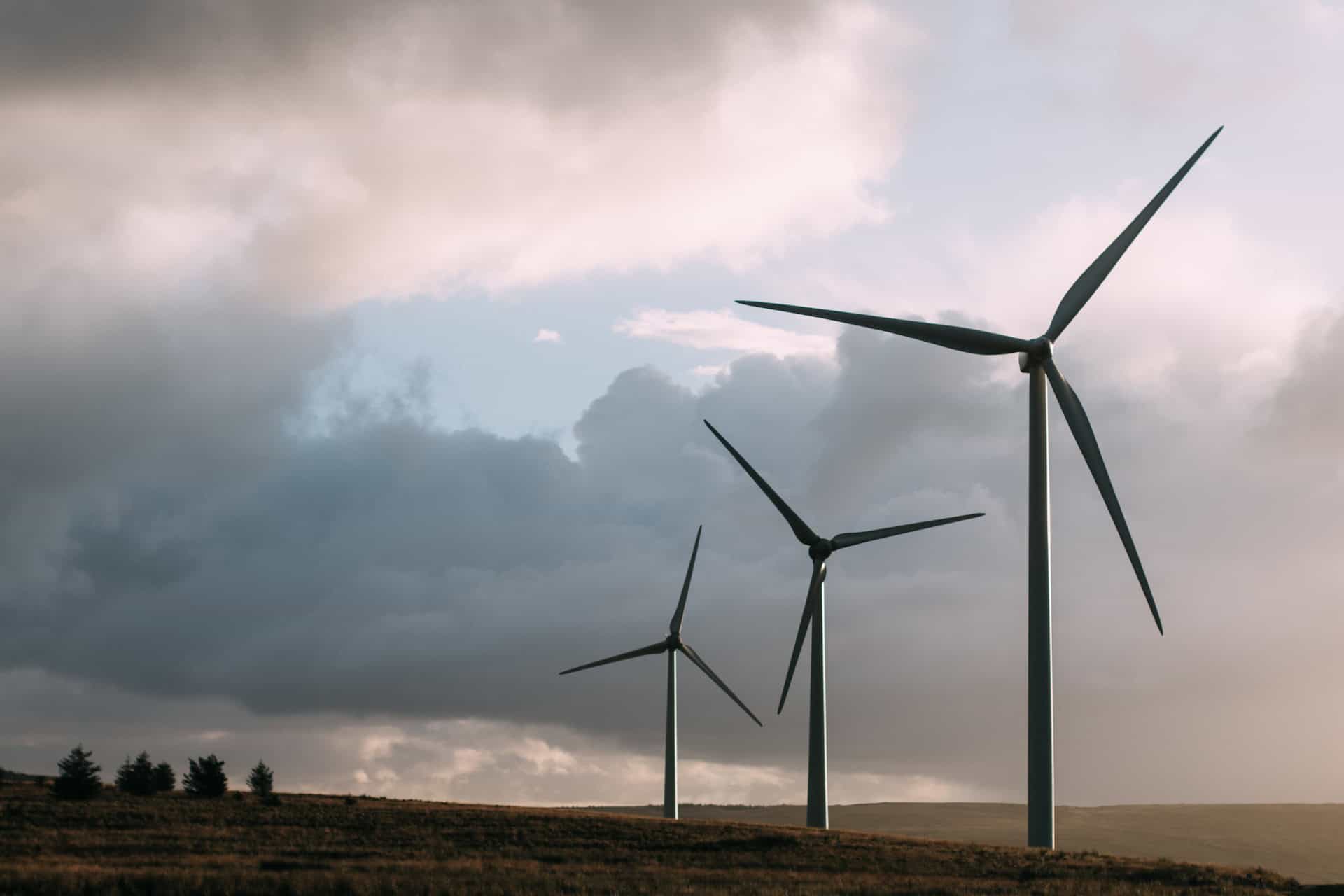 Three wind turbines on a grassy hill under a cloudy sky at sunrise or sunset.