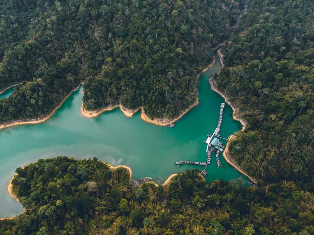 Aerial view of a turquoise lake with a floating village, surrounded by dense green forest.