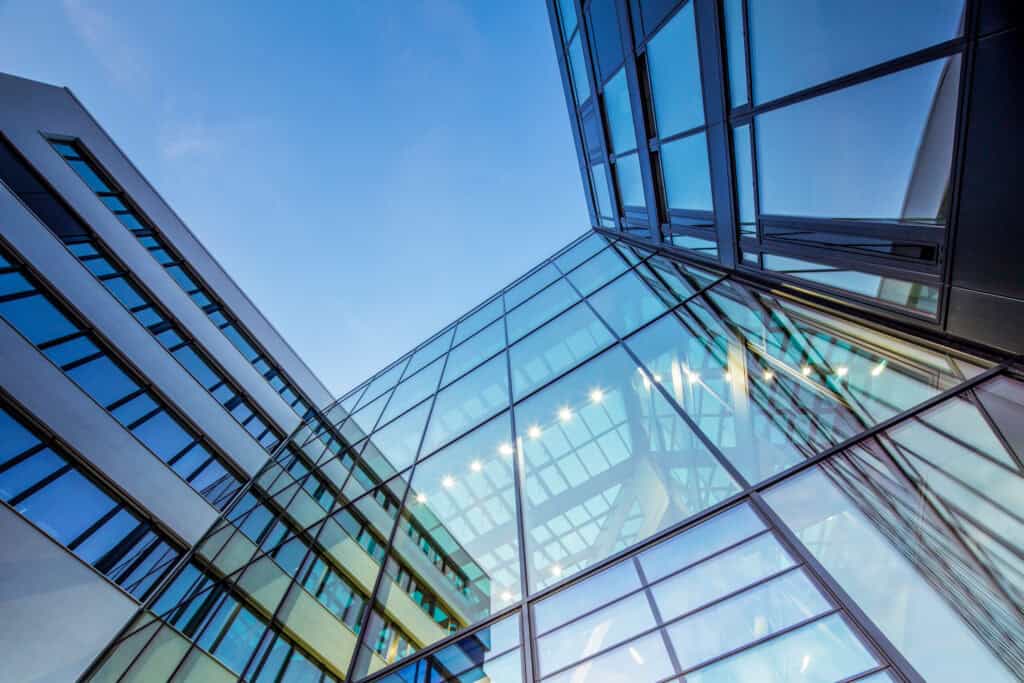 Low-angle view of a modern building with a glass and light-colored facade reflecting the blue sky.