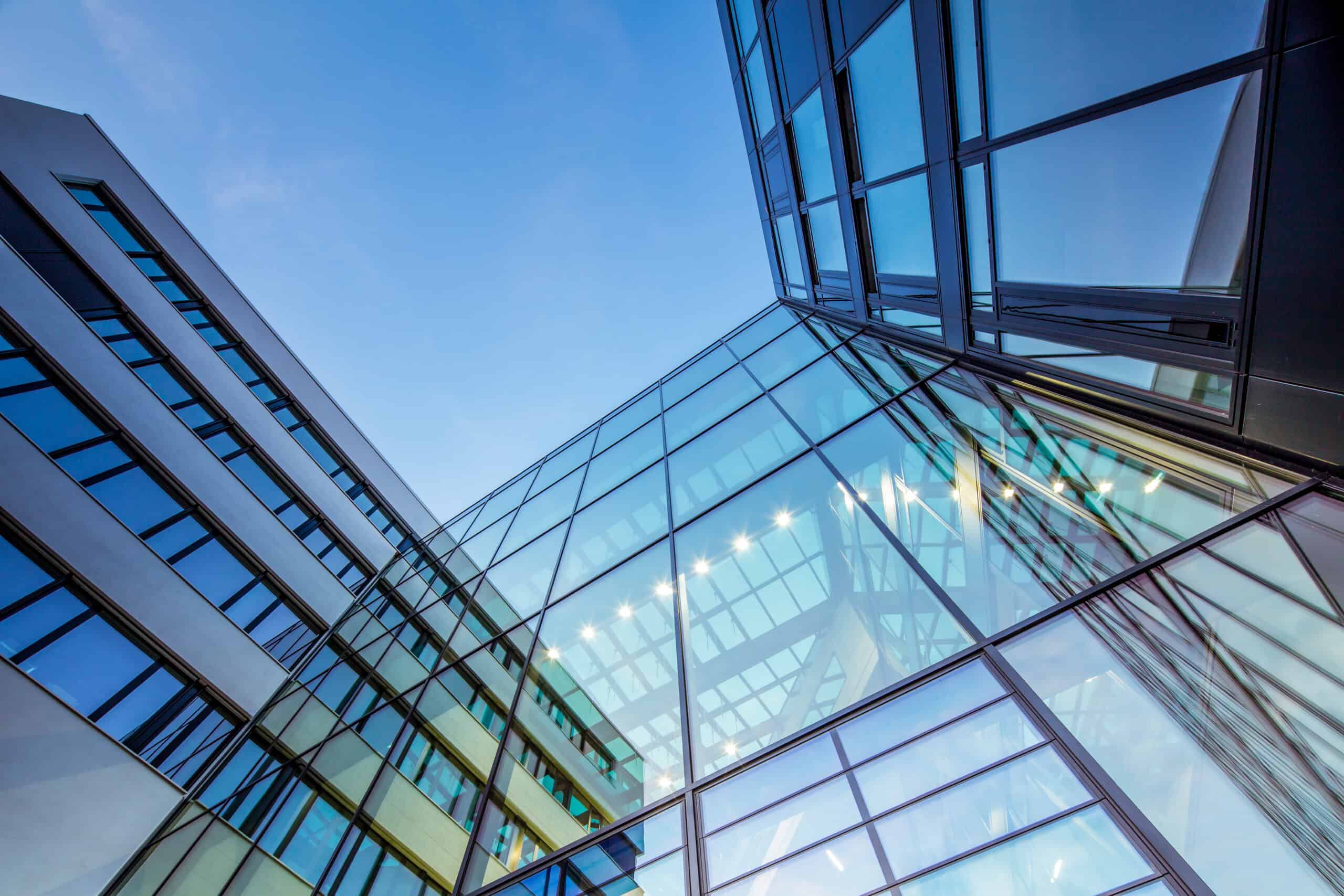 Low-angle view of a modern building with a glass and light-colored facade reflecting the blue sky.