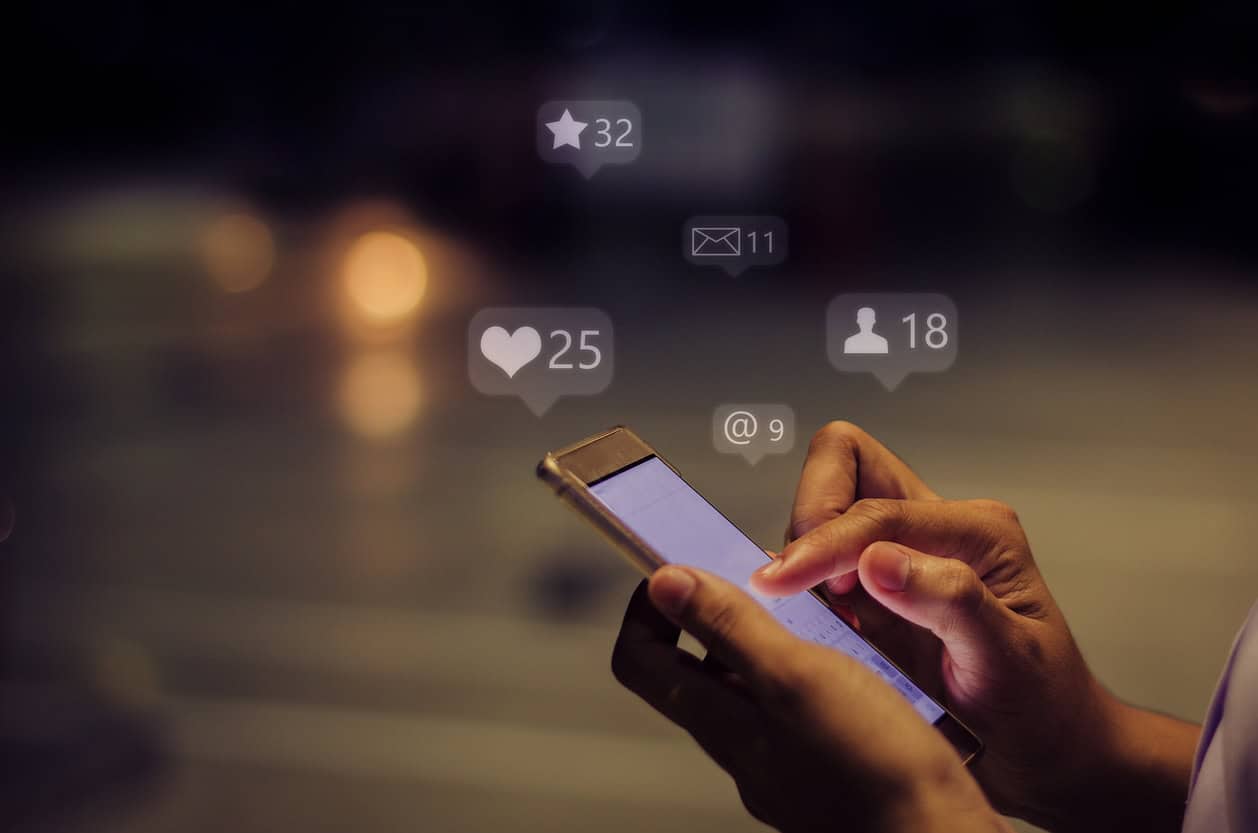 Close-up of hands holding a smartphone with social media notification icons floating above it.