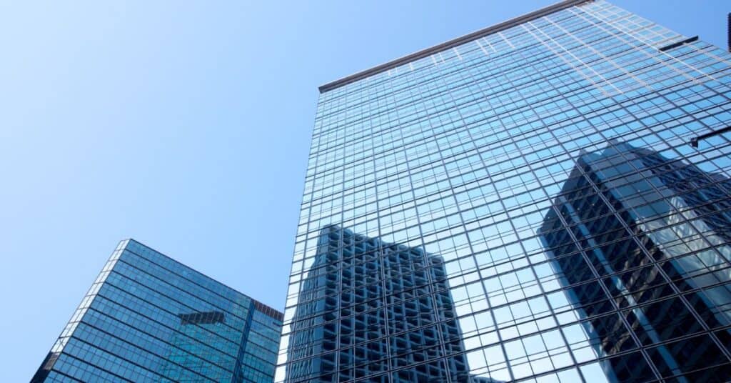 Low-angle view of two modern glass skyscrapers reflecting a clear blue sky and another building.