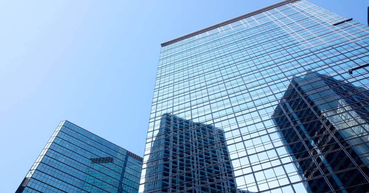 Low-angle view of two modern glass skyscrapers reflecting a clear blue sky and another building.