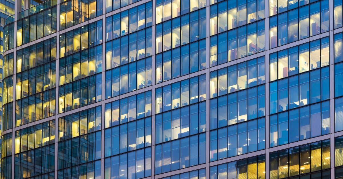 Close-up of a modern glass office building facade with many windows lit up from the inside.