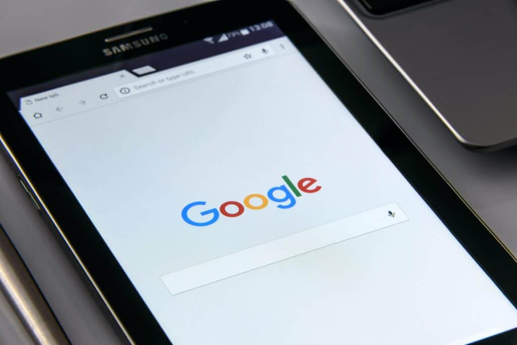 A black Samsung tablet displays the Google search page with its colorful logo and a search bar.