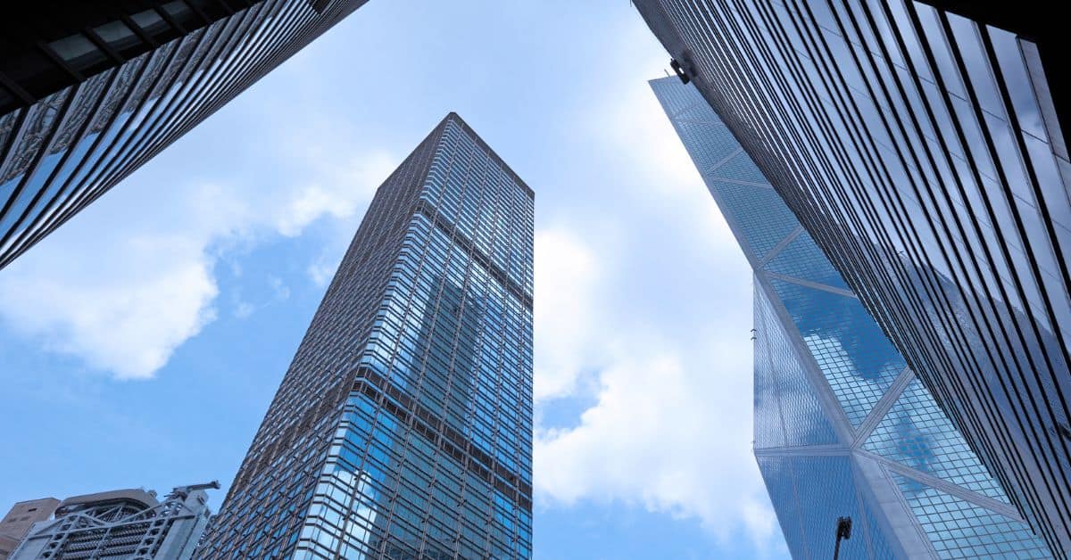 Low-angle view of multiple tall, modern skyscrapers with reflective glass facades against a bright blue sky with white clouds.