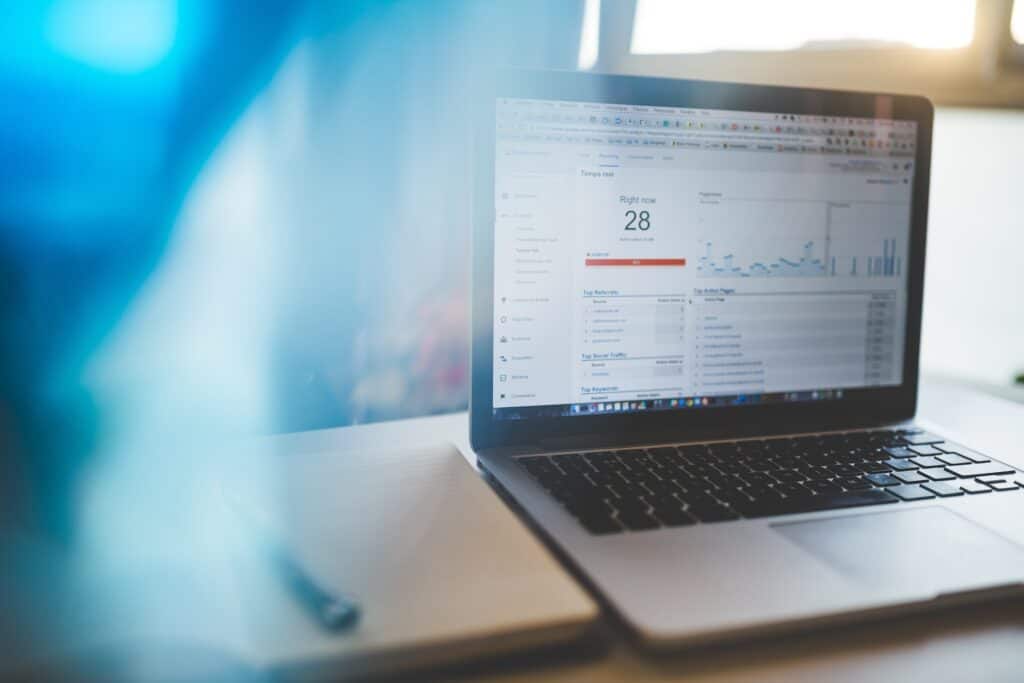 A laptop displaying Google Analytics with 28 active users in real-time, next to a notebook and pen.