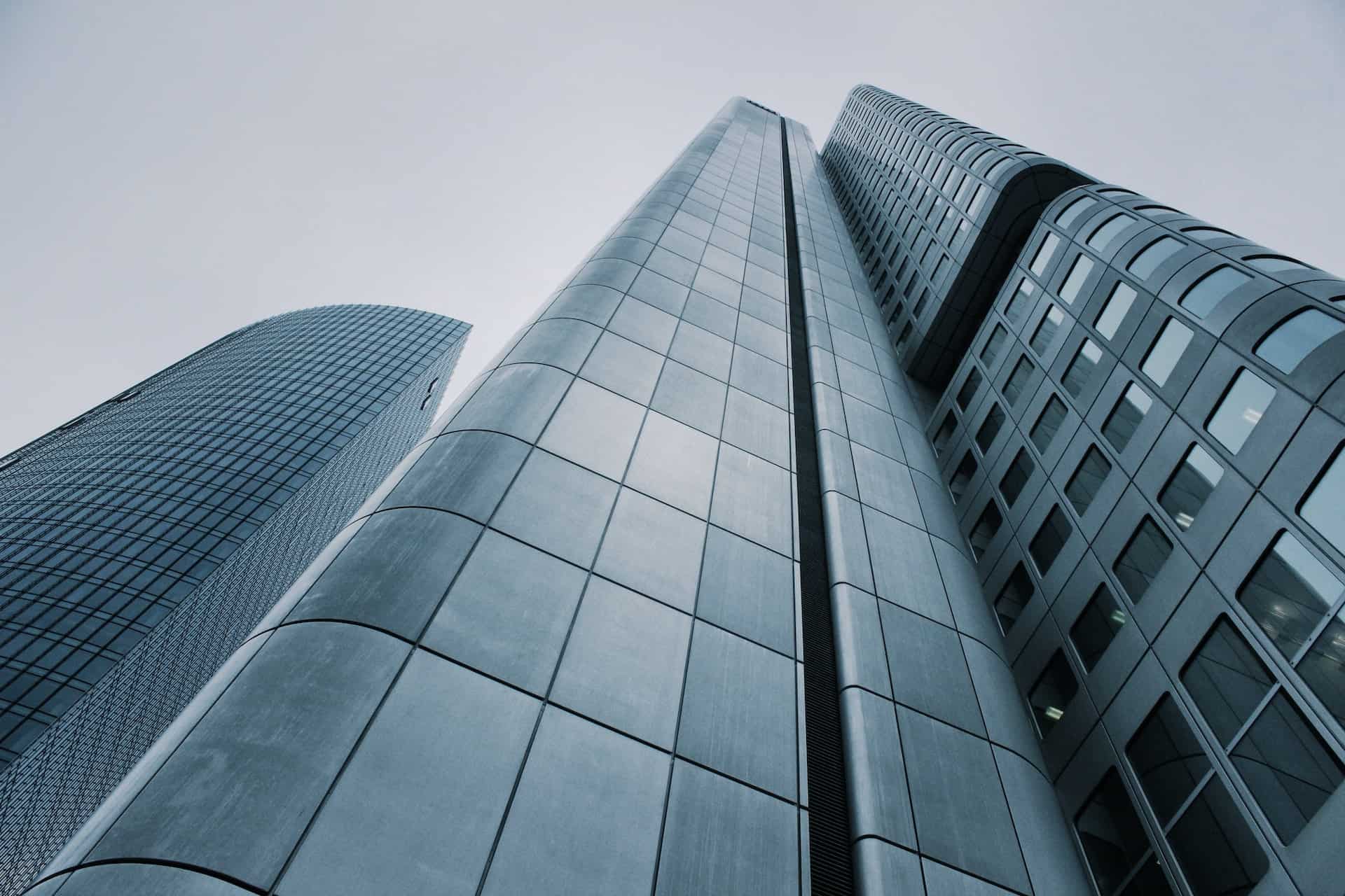 Low-angle view of three modern skyscrapers with glass and metallic facades against a grey sky.