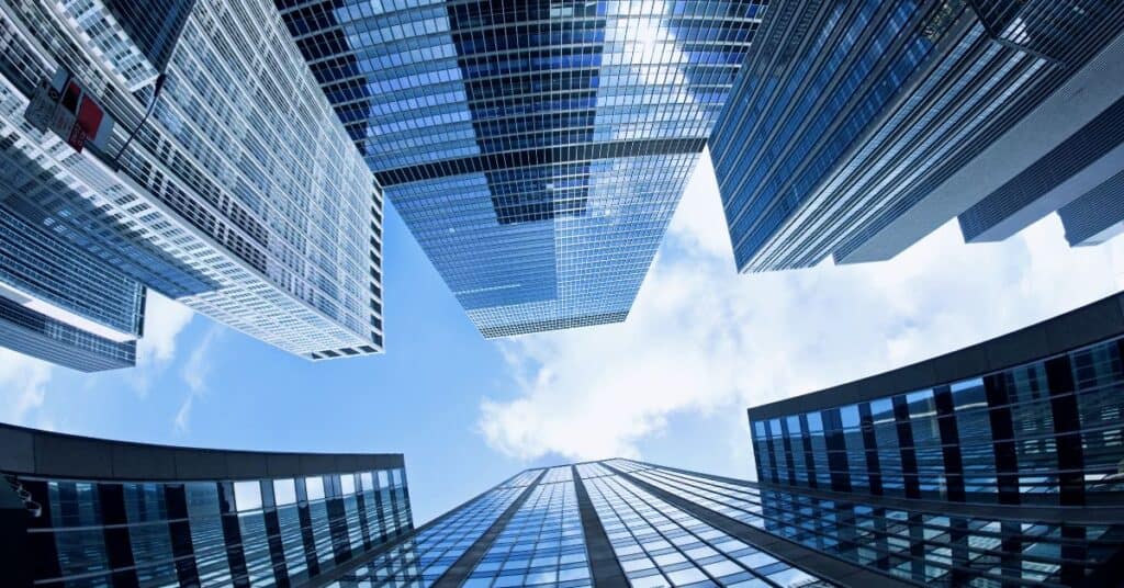 A low-angle view looking up at multiple glass skyscrapers against a blue sky with white clouds.