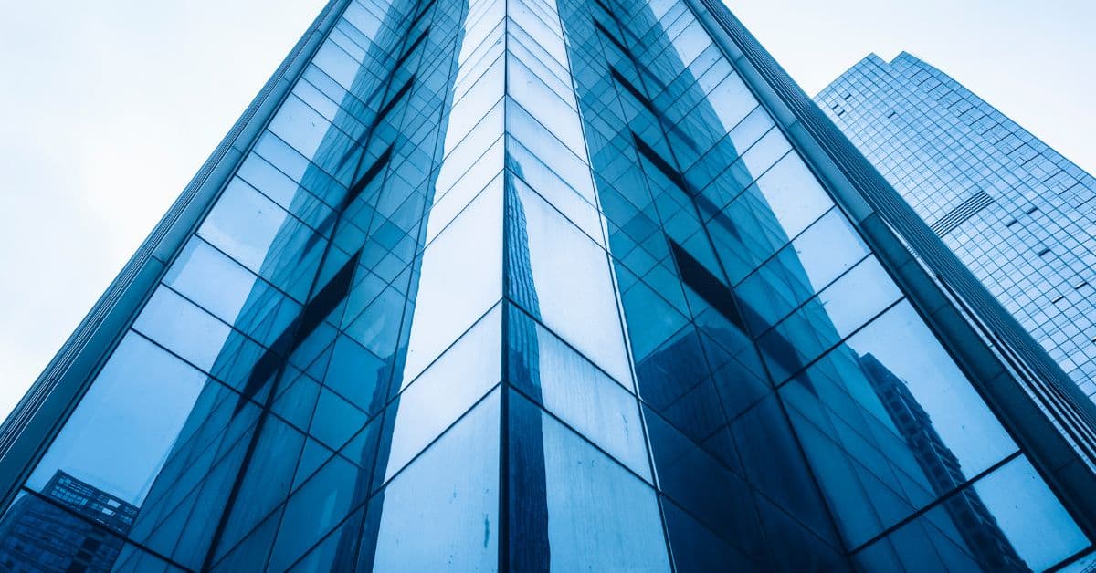 Low-angle view of two tall, blue glass skyscrapers against a bright sky, emphasizing their reflective surfaces and geometric lines.