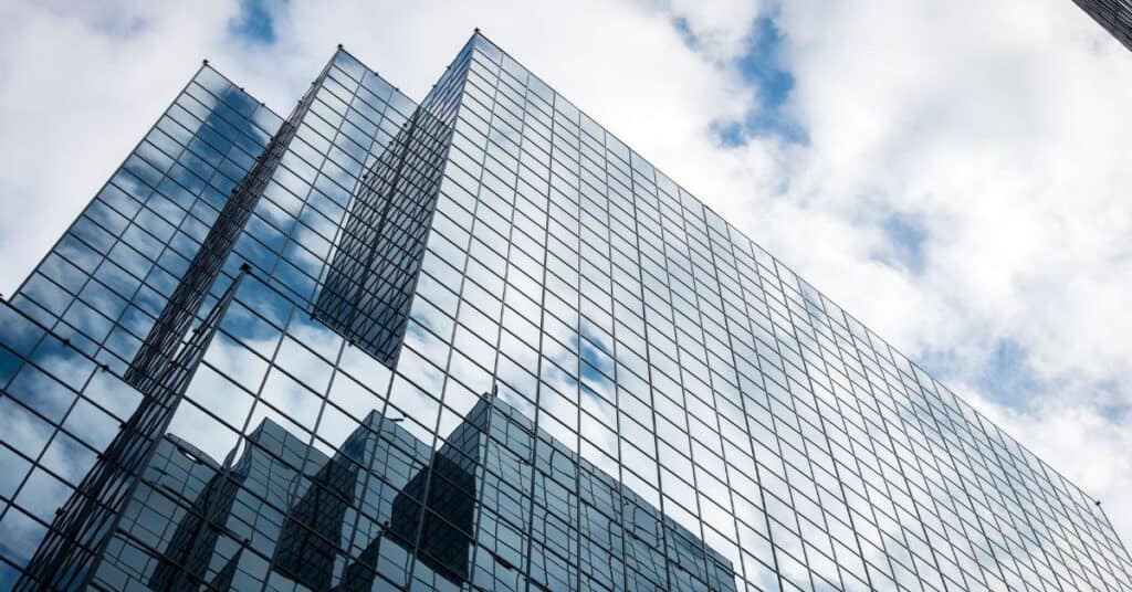 A modern glass building reflecting a cloudy blue sky, viewed from a low angle.