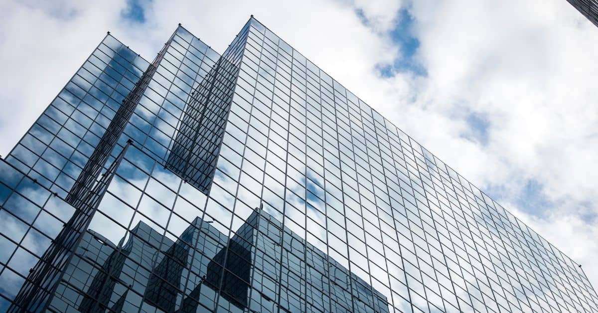 A modern glass building reflecting a cloudy blue sky, viewed from a low angle.