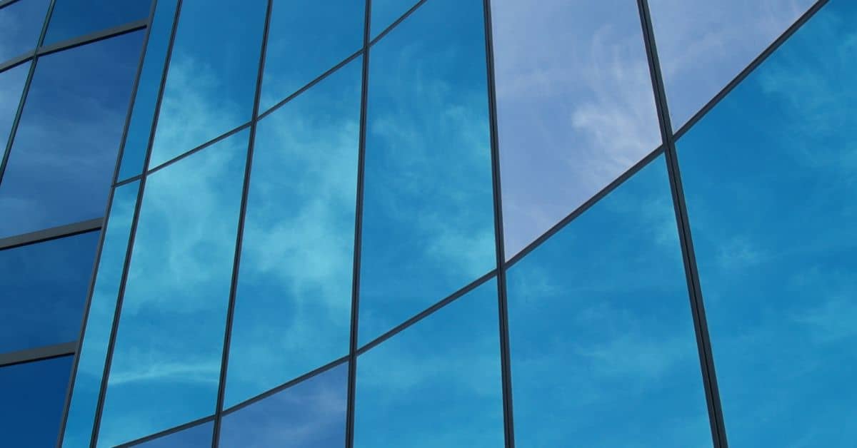 Close-up of a modern building's blue glass facade reflecting a blue sky with white clouds.