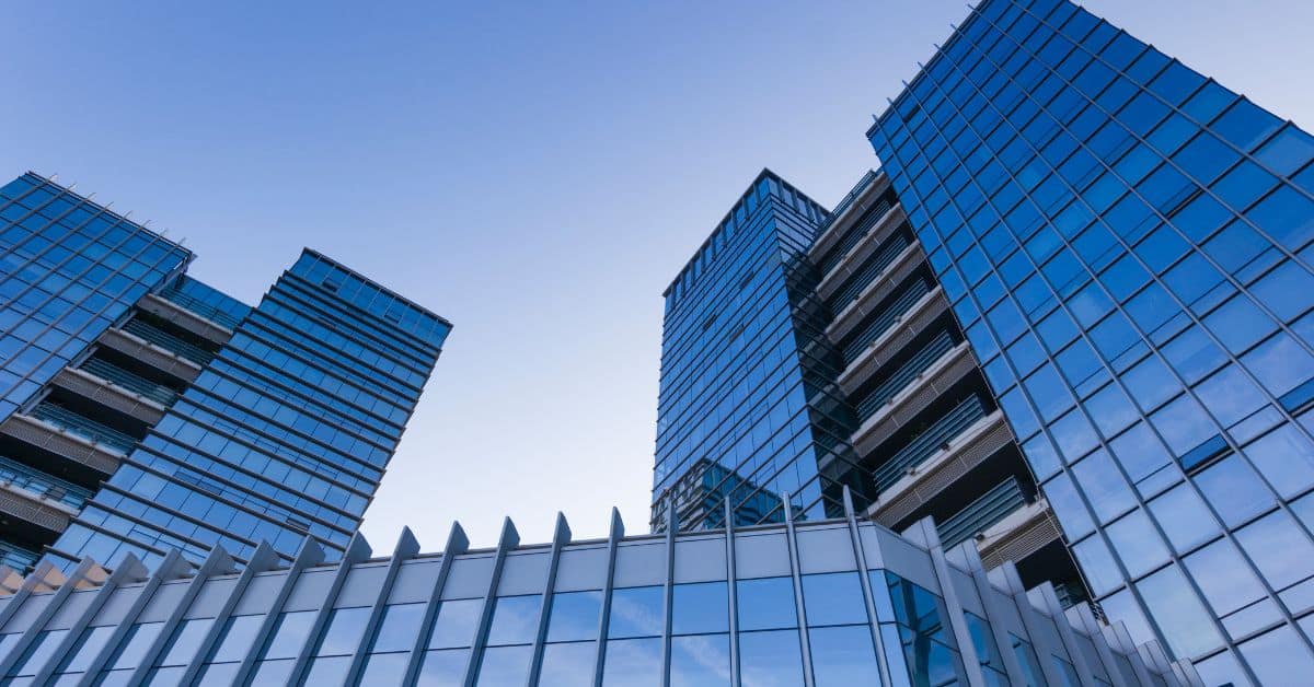 Low-angle view of multiple modern high-rise buildings with blue glass facades under a clear sky.