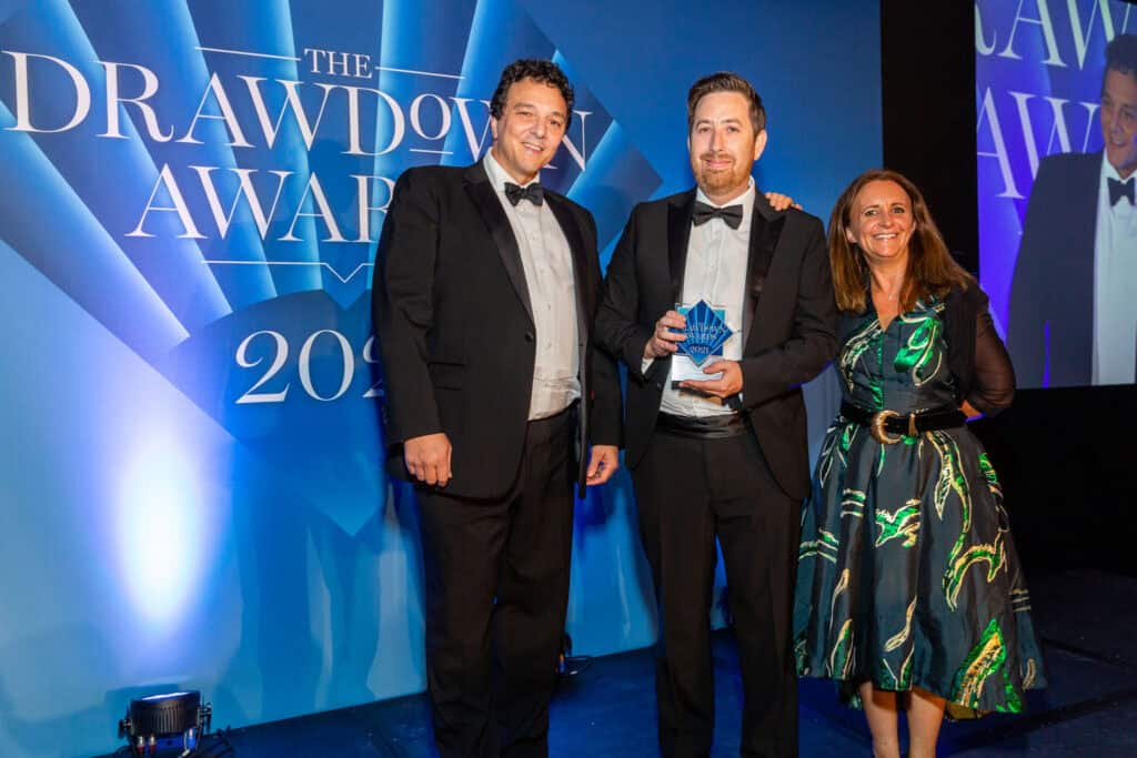 Two men in tuxedos and a woman in a patterned dress stand on stage, holding a star-shaped award at The Drawdown Awards 2021.