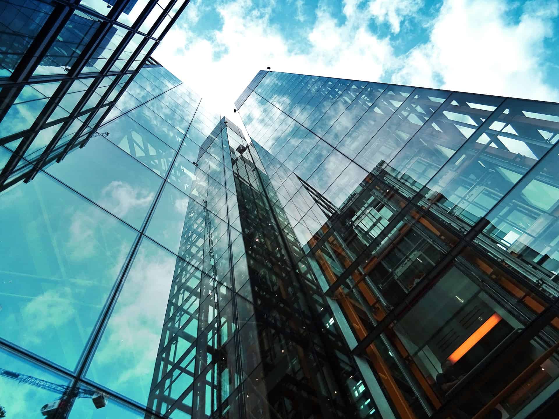 Low-angle view of modern glass skyscrapers reflecting a blue sky with white clouds.