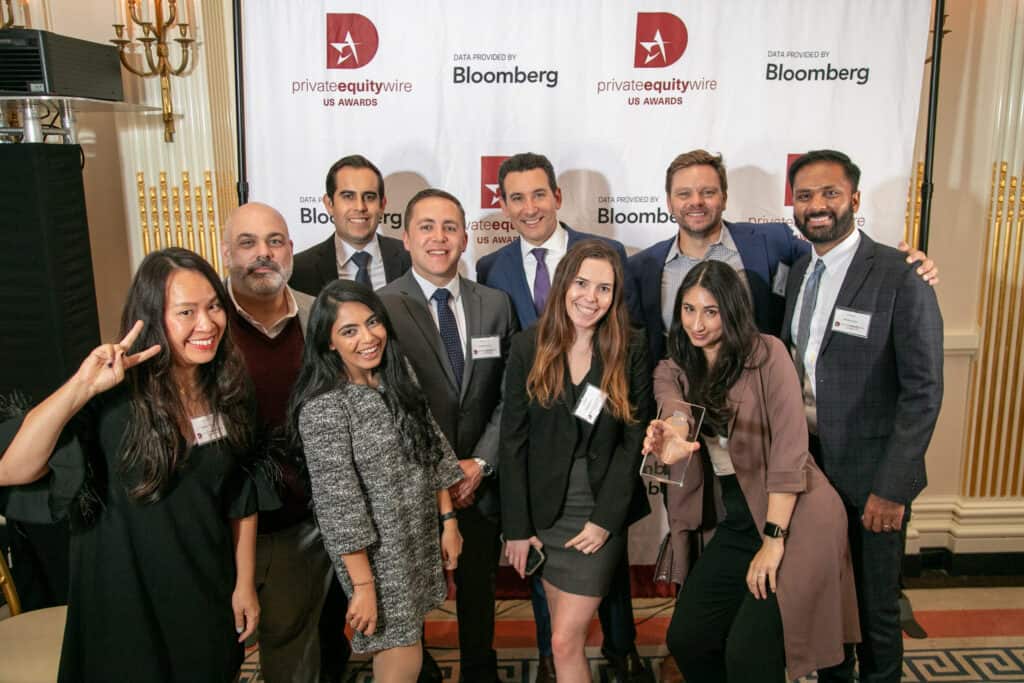 Ten people, six men and four women, smiling and posing in front of a 'privateequitywire US AWARDS' and 'Bloomberg' banner, with one woman holding a clear award.