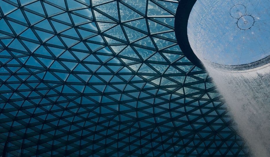 A glass dome ceiling made of triangular panels, with a large waterfall cascading from a circular opening in the upper right.