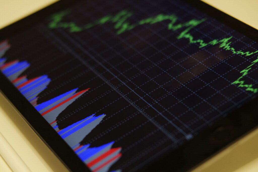 A tablet screen displaying a green line graph and blue and red bar charts on a dark grid background, with a white stylus nearby.