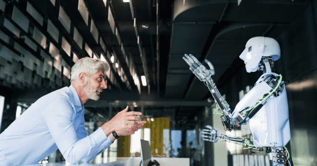 A man with gray hair and a beard smiles while interacting with a white humanoid robot with glowing features and exposed wiring.