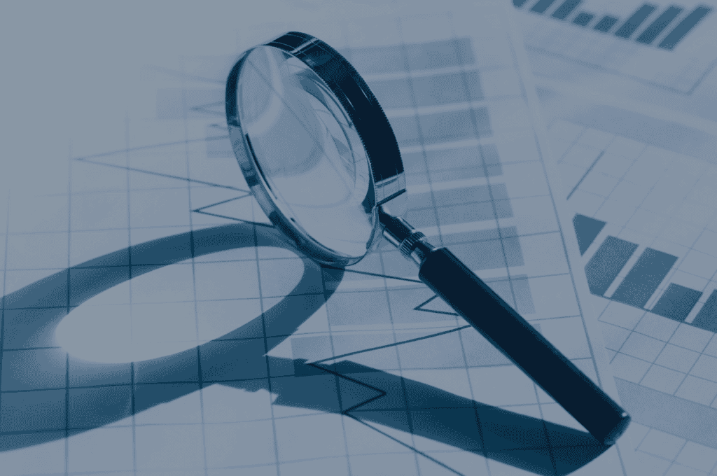 A magnifying glass rests on blue-toned documents displaying charts and graphs, symbolizing data analysis.