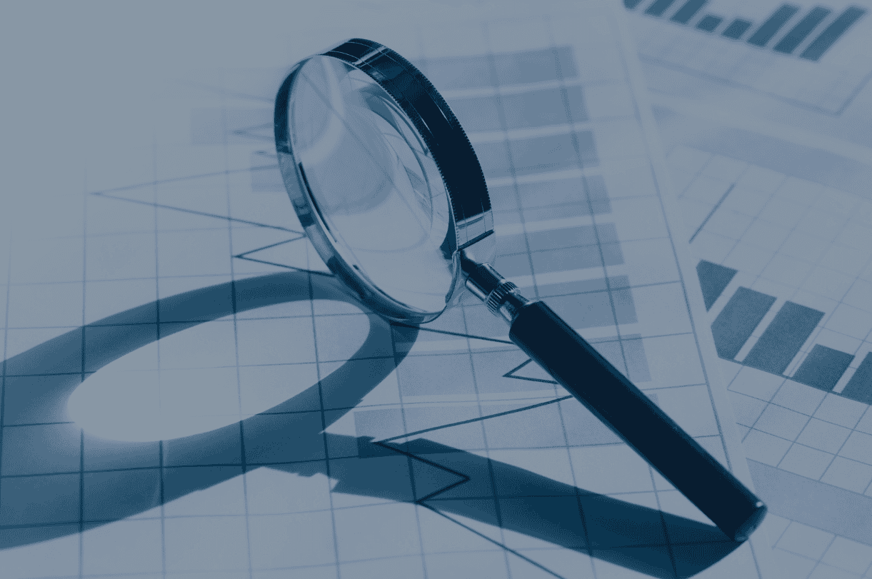 A magnifying glass rests on blue-toned documents displaying charts and graphs, symbolizing data analysis.