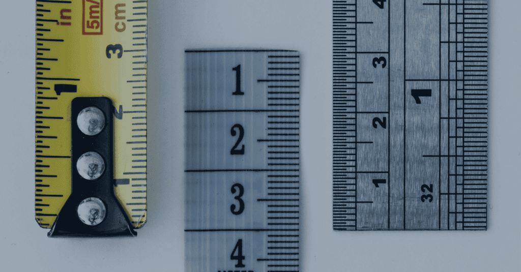 Three measuring tools: a yellow tape measure, a translucent fabric tape, and a metal ruler, displayed vertically side-by-side on a light background.