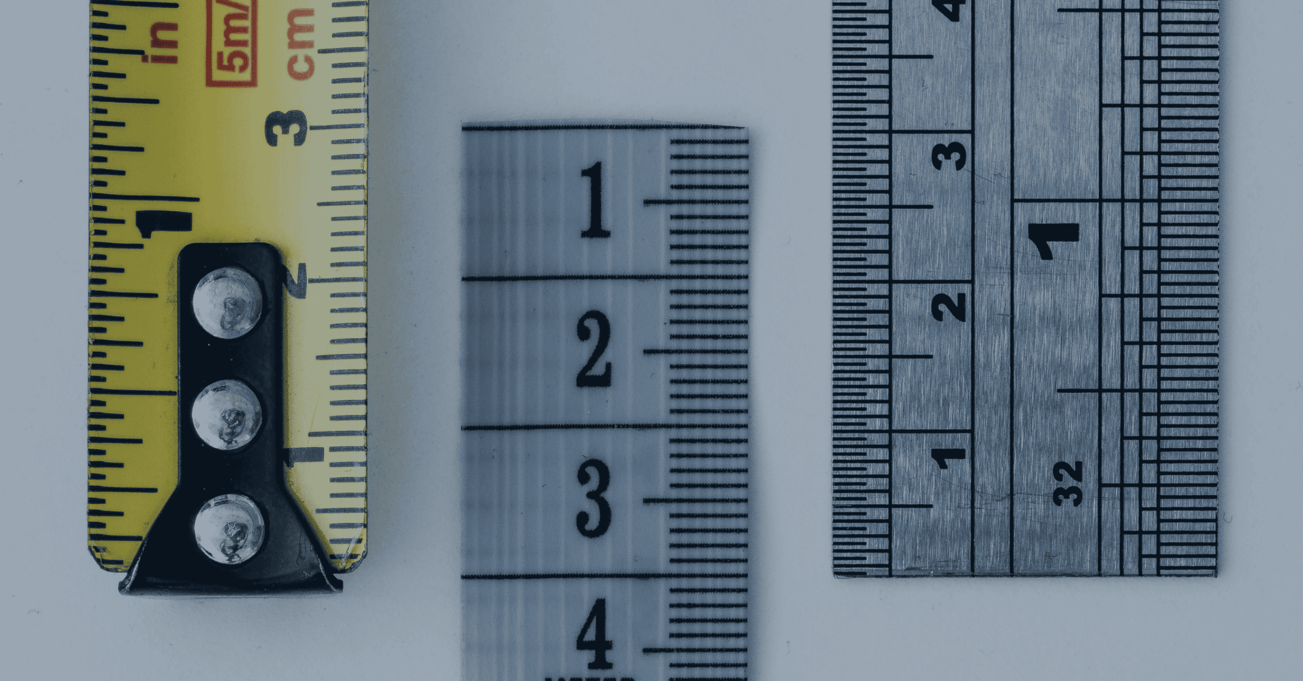 Three measuring tools: a yellow tape measure, a translucent fabric tape, and a metal ruler, displayed vertically side-by-side on a light background.