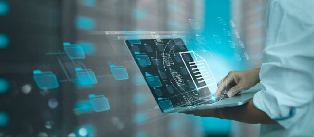 A person's hands using a laptop, surrounded by glowing blue holographic folder and document icons, symbolizing digital data management.