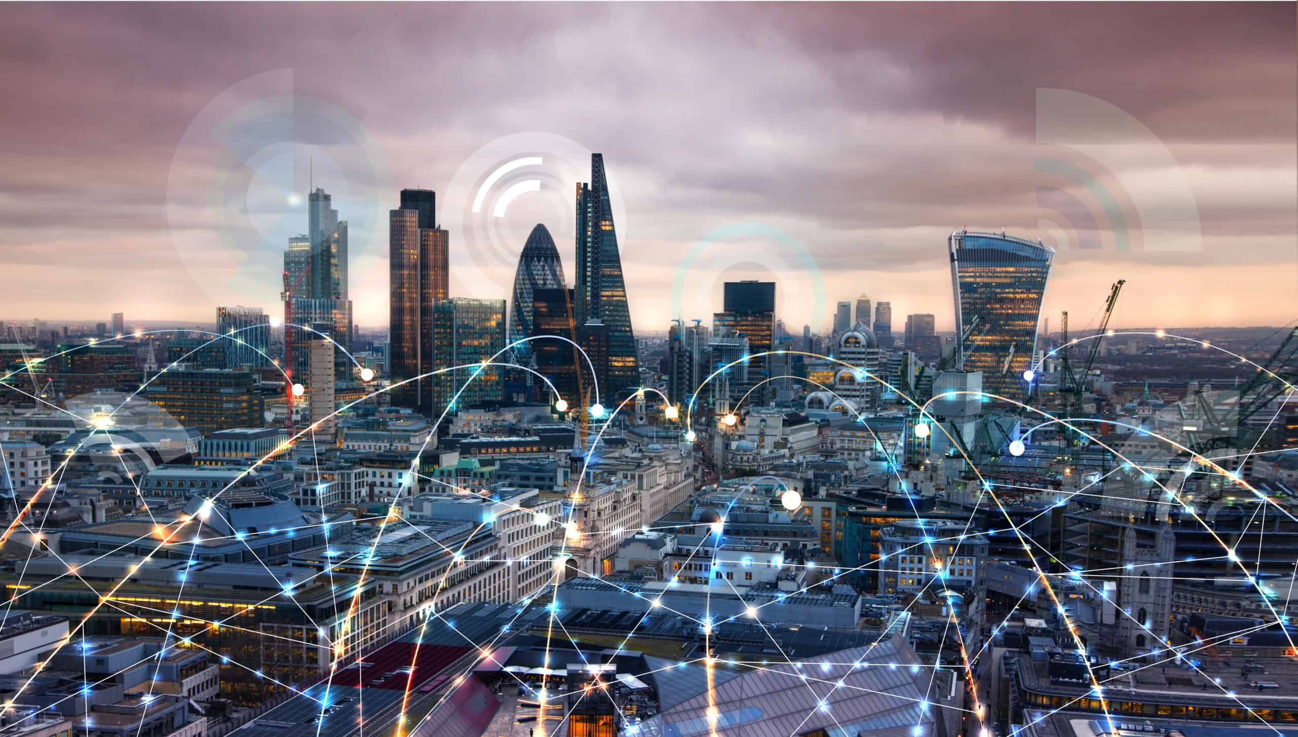 Aerial view of a city skyline at dusk with glowing digital network lines connecting buildings and signal graphics in the sky.