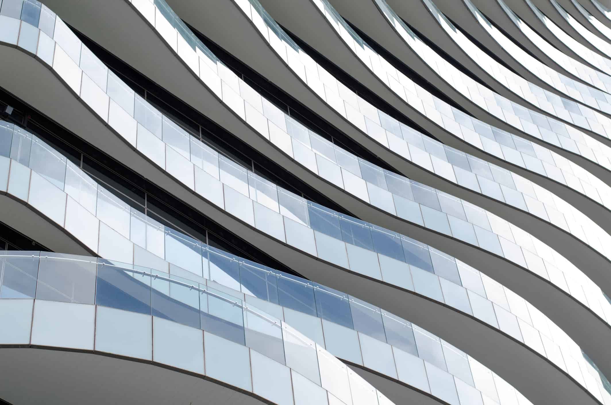 Close-up of a modern building facade with undulating white balconies and glass railings.