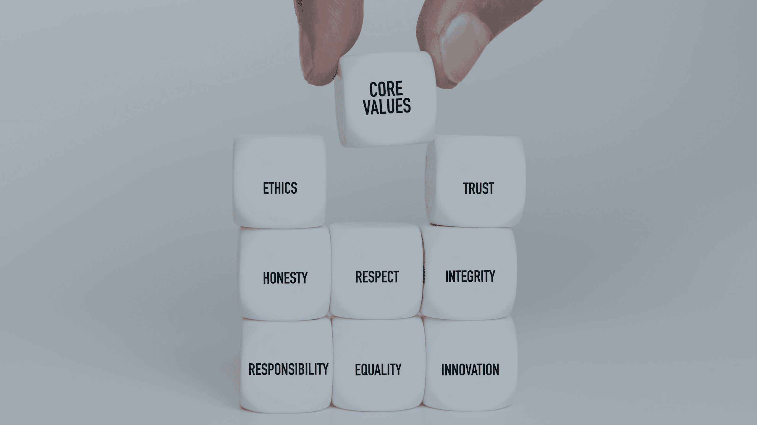 A hand places a die labeled 'CORE VALUES' on top of a stack of dice with words like 'ETHICS', 'TRUST', 'HONESTY', 'RESPECT', 'INTEGRITY', 'RESPONSIBILITY', 'EQUALITY', and 'INNOVATION'.