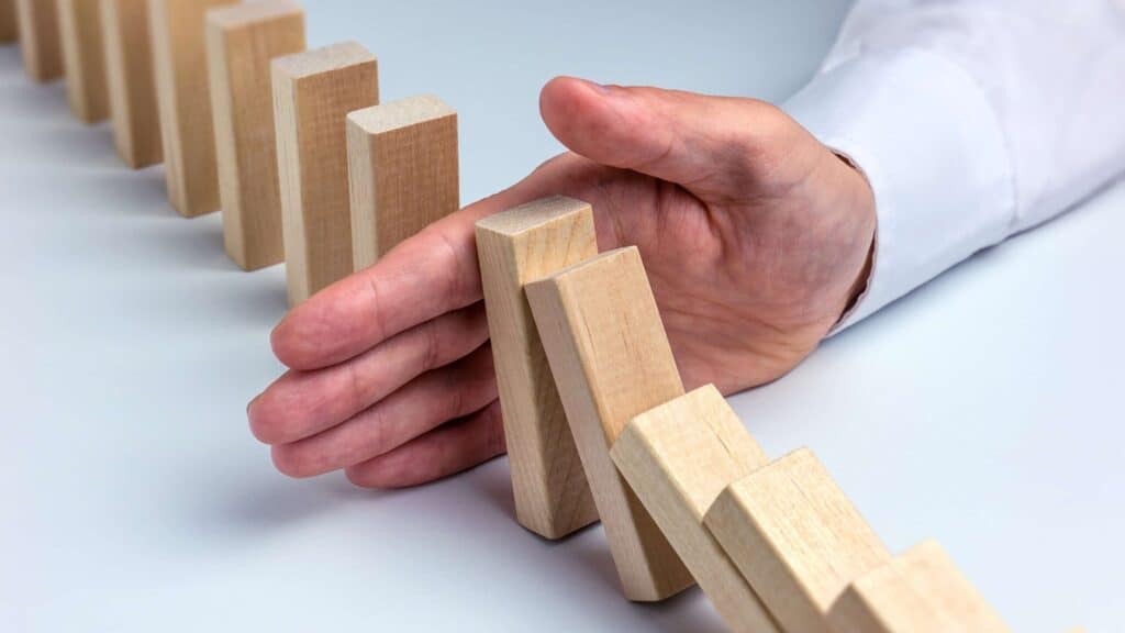 A person's hand in a white shirt cuff stops a line of falling wooden domino blocks.