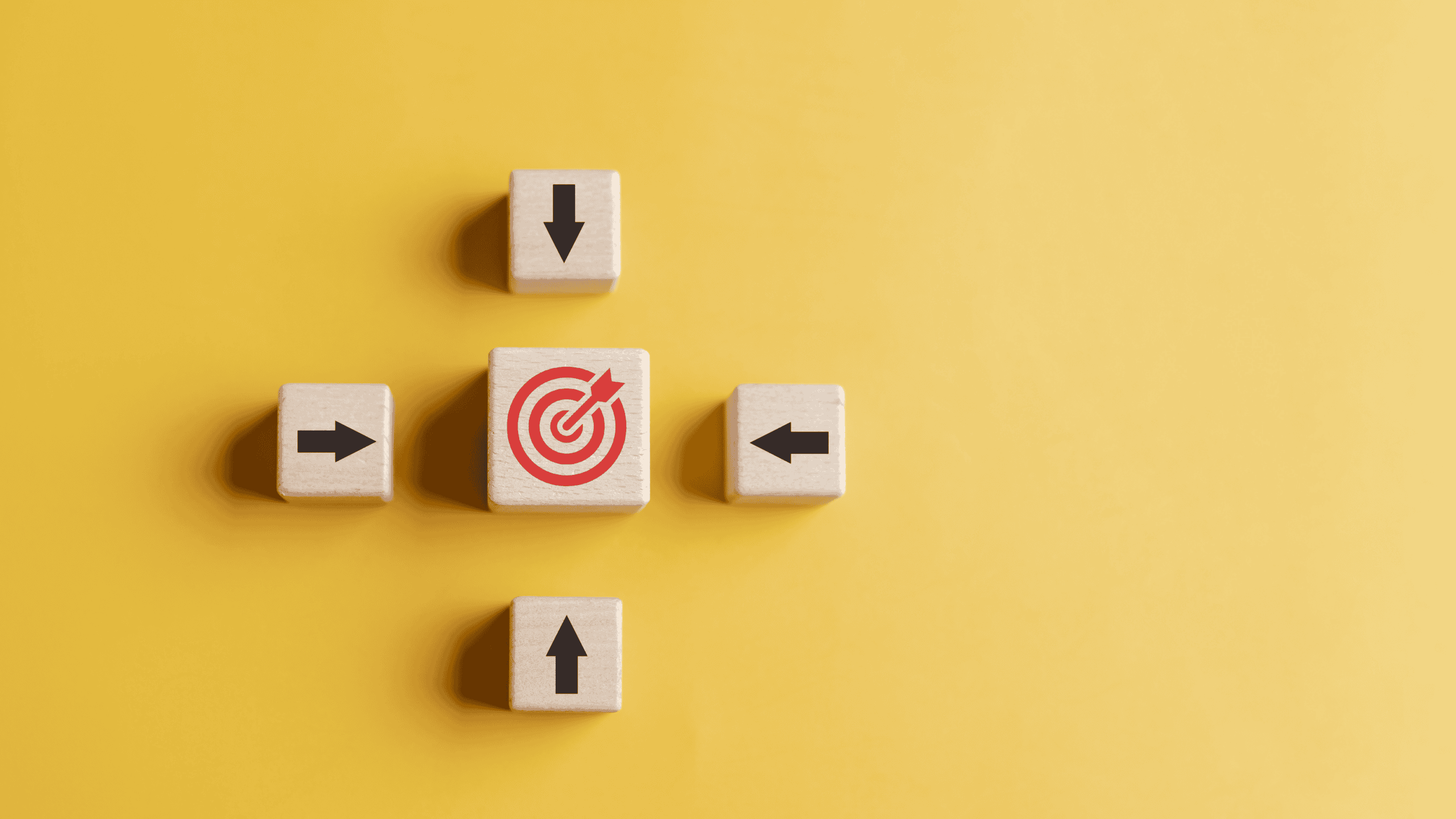 Five wooden blocks on a yellow background. A central block shows a red target with an arrow, surrounded by four blocks with black arrows pointing towards the center.